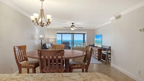 A dining area with a round table and chairs, a chandelier, and a view of the ocean through large windows.