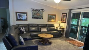 A living room with a black leather sectional sofa, a round wooden coffee table, and a glass door leading to a deck. - 15 PRIVATE ACRES !! WATERFRONT, SWIMMING POOL !! HOT TUB !!  PETS WELCOME TOO !! (RICHFIELD)