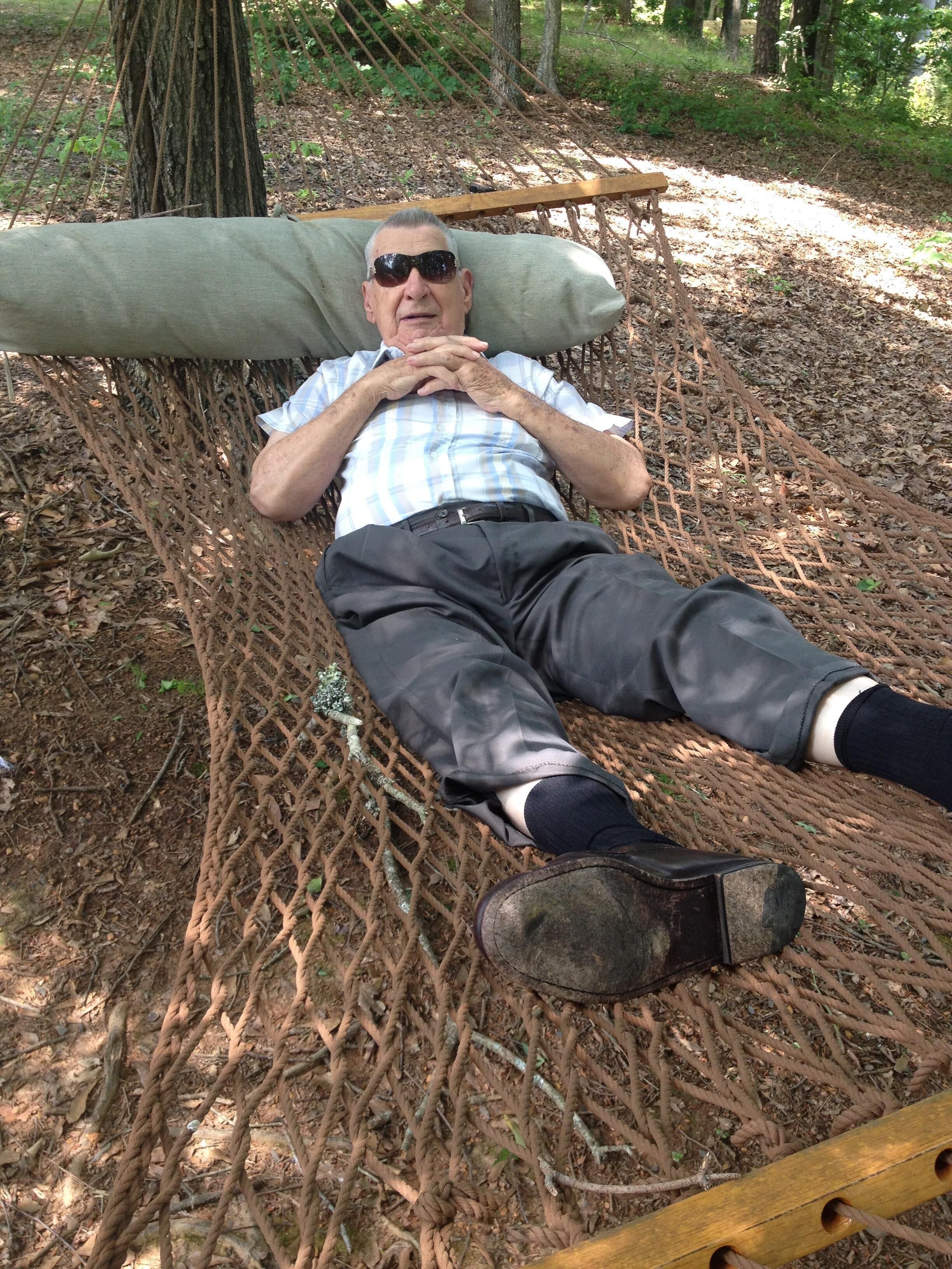 A person lying on a hammock in a wooded area.