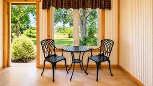 Una habitación con un revestimiento de madera, una ventana con vistas a follaje, y dos sillas de metal negro alrededor de una pequeña mesa redonda.