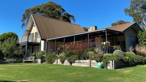 A two-story house with a sloped roof, a balcony on the upper floor, and a garden with various plants and a hose. - Mon Desir - Yarra Valley (Yarra Ranges)