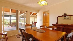 A dining room with a wooden table and chairs, a chandelier, and a view through large sliding glass doors to an outdoor patio. - Mon Desir - Yarra Valley (Yarra Ranges)