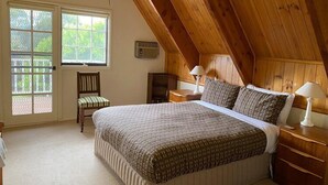 A bedroom with a sloped ceiling, a bed with patterned bedding, two bedside tables with lamps, a chair, and a window with a view of greenery. - Mon Desir - Yarra Valley (Yarra Ranges)