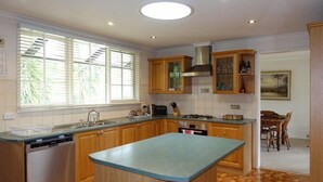 A kitchen with wooden cabinets, a central island, a built-in oven, and a window with blinds. - Mon Desir - Yarra Valley (Yarra Ranges)