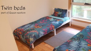 Zwei Betten mit floraler Bettwäsche in einem Zimmer mit Holzboden und einem Fenster.