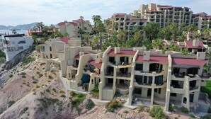 A coastal hotel with multiple-story buildings, balconies, and a rocky hillside. - Casa Mar Azul, a Stunning Oceanfront Condo (Cabo San Lucas)