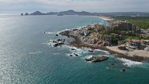 A coastal hotel with multiple buildings, a rocky shoreline, and a beach in the background. - Casa Mar Azul, a Stunning Oceanfront Condo (Cabo San Lucas)