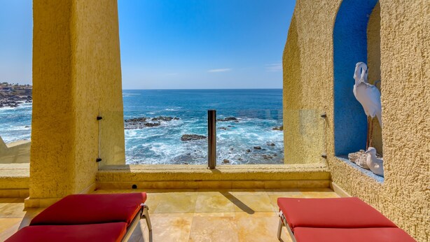 A seaside view from a balcony with red chairs, a stone wall, and a seagull statue. - Casa Mar Azul, a Stunning Oceanfront Condo (Cabo San Lucas)