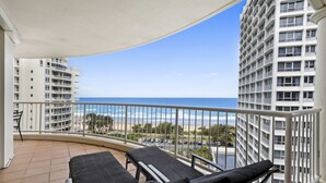 Ein Balkon mit zwei Liegestühlen, Blick auf den Strand und hohe Gebäude im Hintergrund.