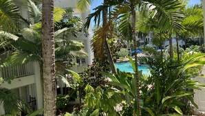 Une piscine entourée d’une végétation tropicale luxuriante et un immeuble à plusieurs étages doté de balcons.