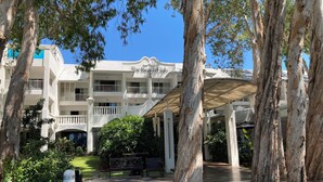 Un bâtiment appelé « The Beach Club », doté d’une entrée couverte, entouré d’arbres et agrémenté d’un panneau indiquant « Stationnement interdit ».