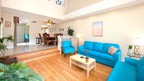 Amplia sala de estar con un sofá azul, una mesa de centro de madera y un comedor al fondo.