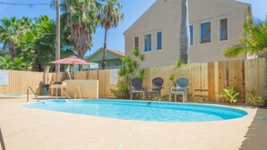 Una piscina con cubierta de madera, sillas y valla de madera.