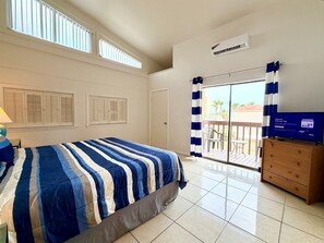 A hotel room with a bed, a TV, a dresser, and a balcony with a view.