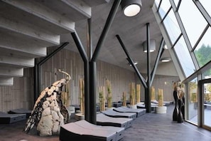 A modern interior with a unique architectural design, featuring a large rock sculpture, lounge areas, and a view through large windows. - Hotel Breza (Podcetrtek)