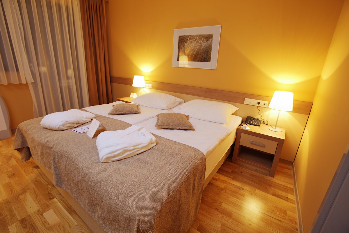 A hotel room with a large bed, two bedside tables, a nightstand, and a wall-mounted lamp.