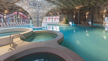 Una piscina interior con múltiples carriles, un elemento acuático central y zonas de descanso con asientos.