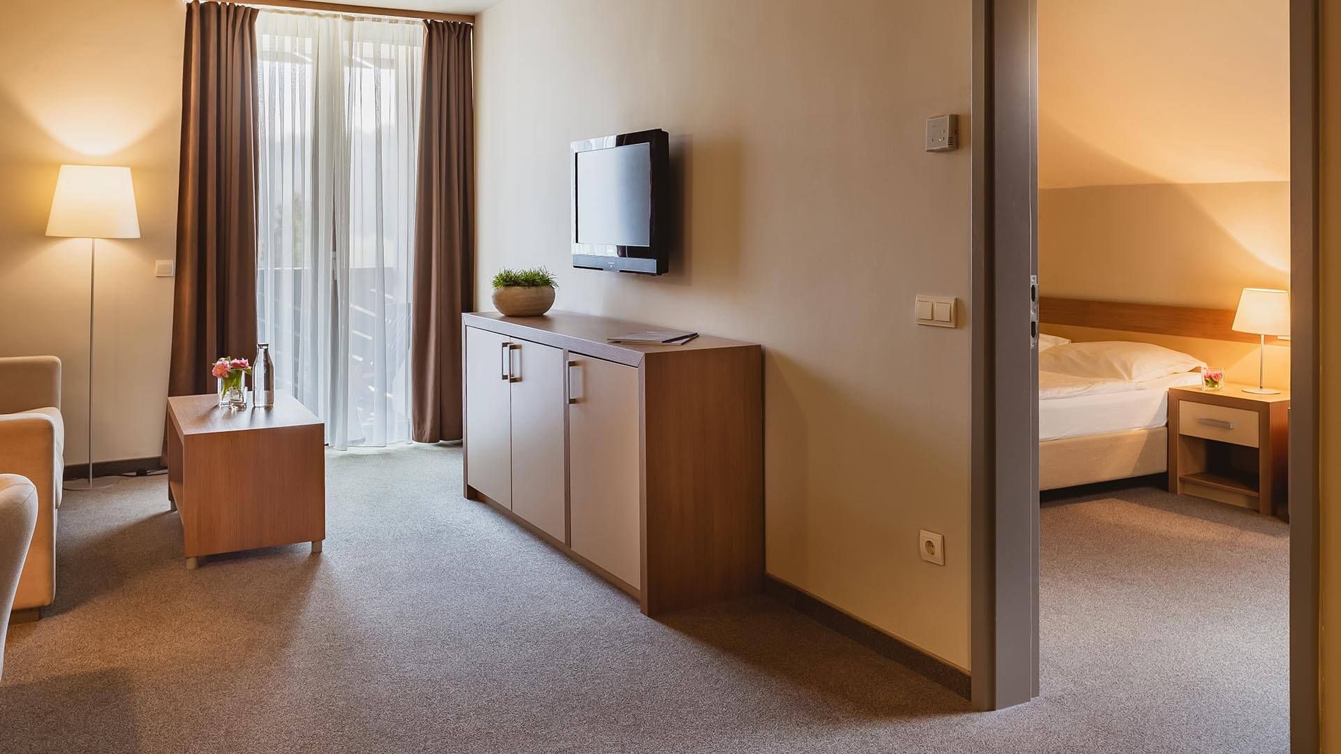 Ein Hotelzimmer mit einem Bett, Nachttisch, Lampe und einem an der Wand befestigten Fernseher.