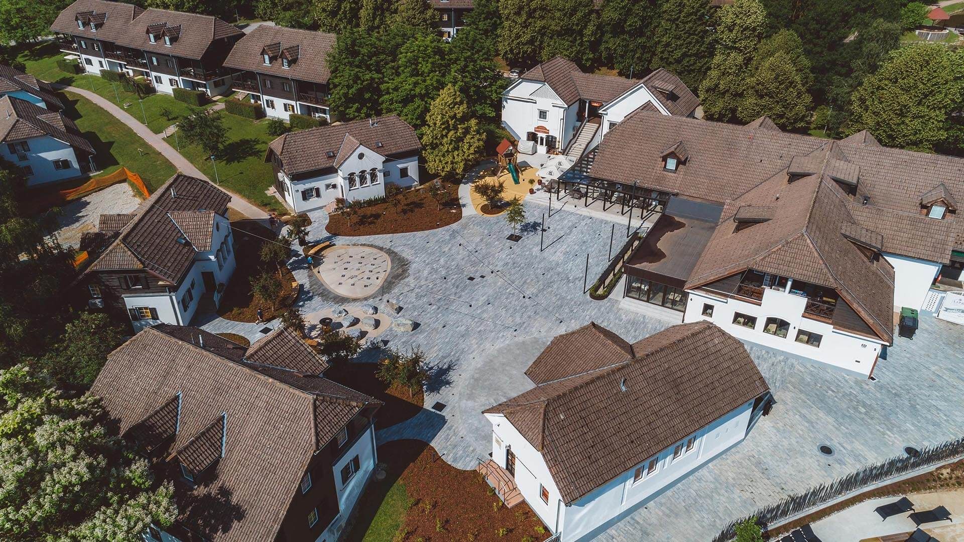 An aerial view of a residential area with multiple houses, a central courtyard, and surrounding greenery.