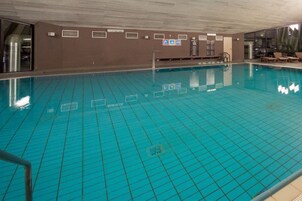 Una piscina interior con carriles delimitados, una silla de salvavidas y un área de descanso con sillones.