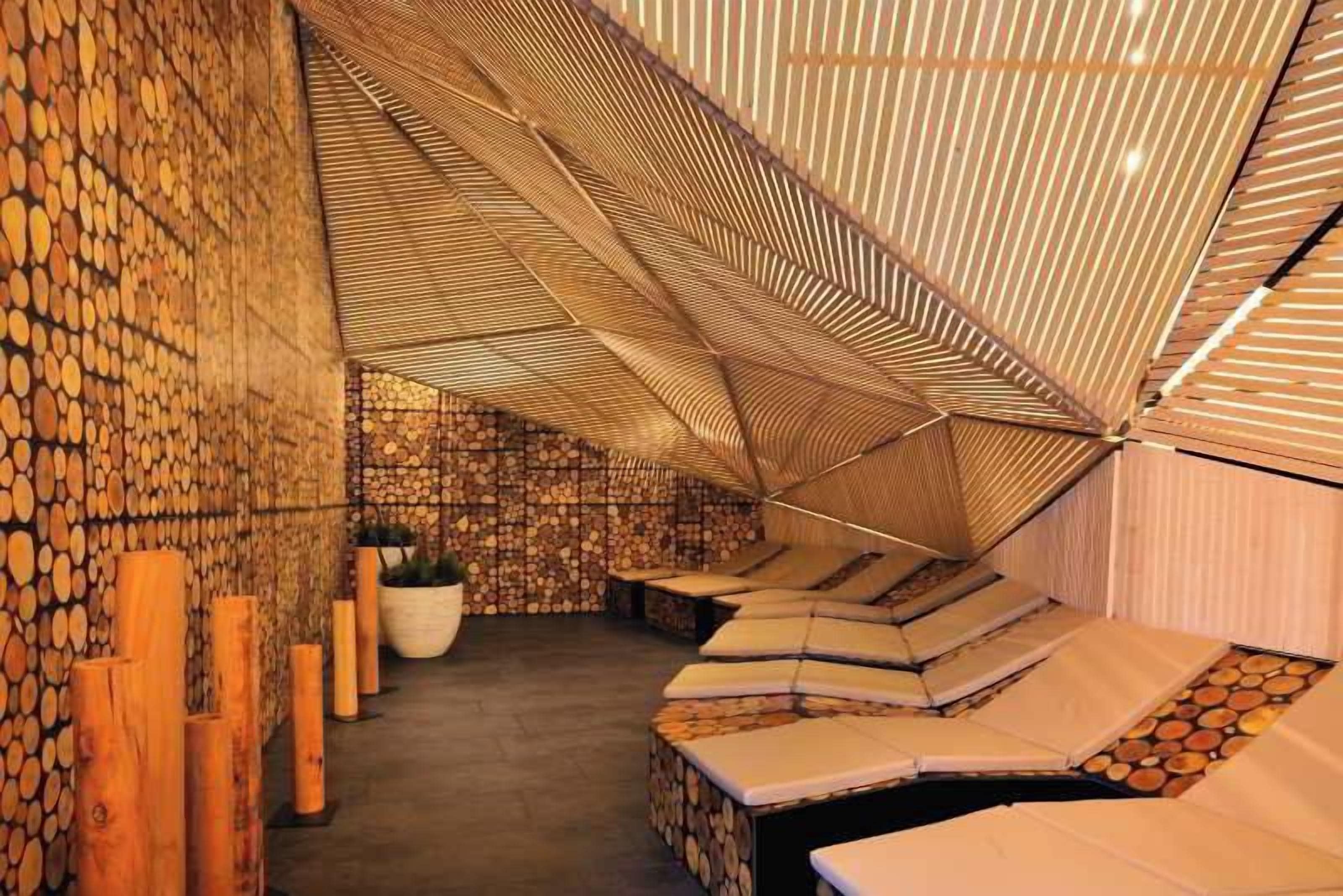 Una habitación con techo inclinado, troncos de madera en las paredes y una zona de estar con cojines.