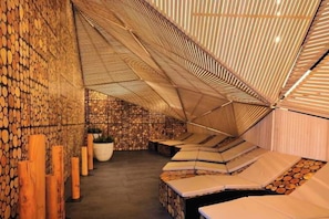 A room with a sloped ceiling, wooden logs on the walls, and a seating area with cushions. - Hotel Breza (Podcetrtek)