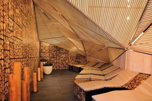 Una habitación con techo inclinado, troncos de madera en las paredes y una zona de estar con cojines.