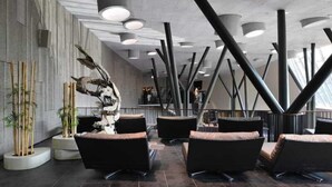 Ein modernes Interieur mit schwarzen Stühlen, einer zentralen Skulptur und einer hohen Decke mit freiliegenden Balken.