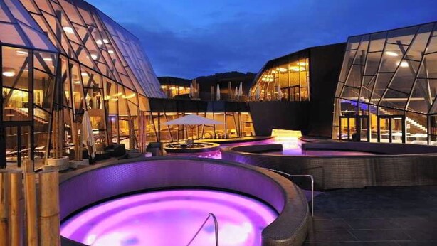 Un edifici modern amb façanes de vidre i una zona de piscina exterior amb aigua calenta.