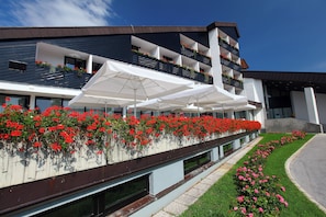 Un hotel moderno con un balcón decorado con flores rojas, sombrillas blancas y un césped cuidado.