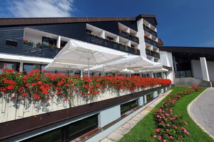 Un hotel moderno con un balcón decorado con flores rojas, sombrillas blancas y un césped cuidado.