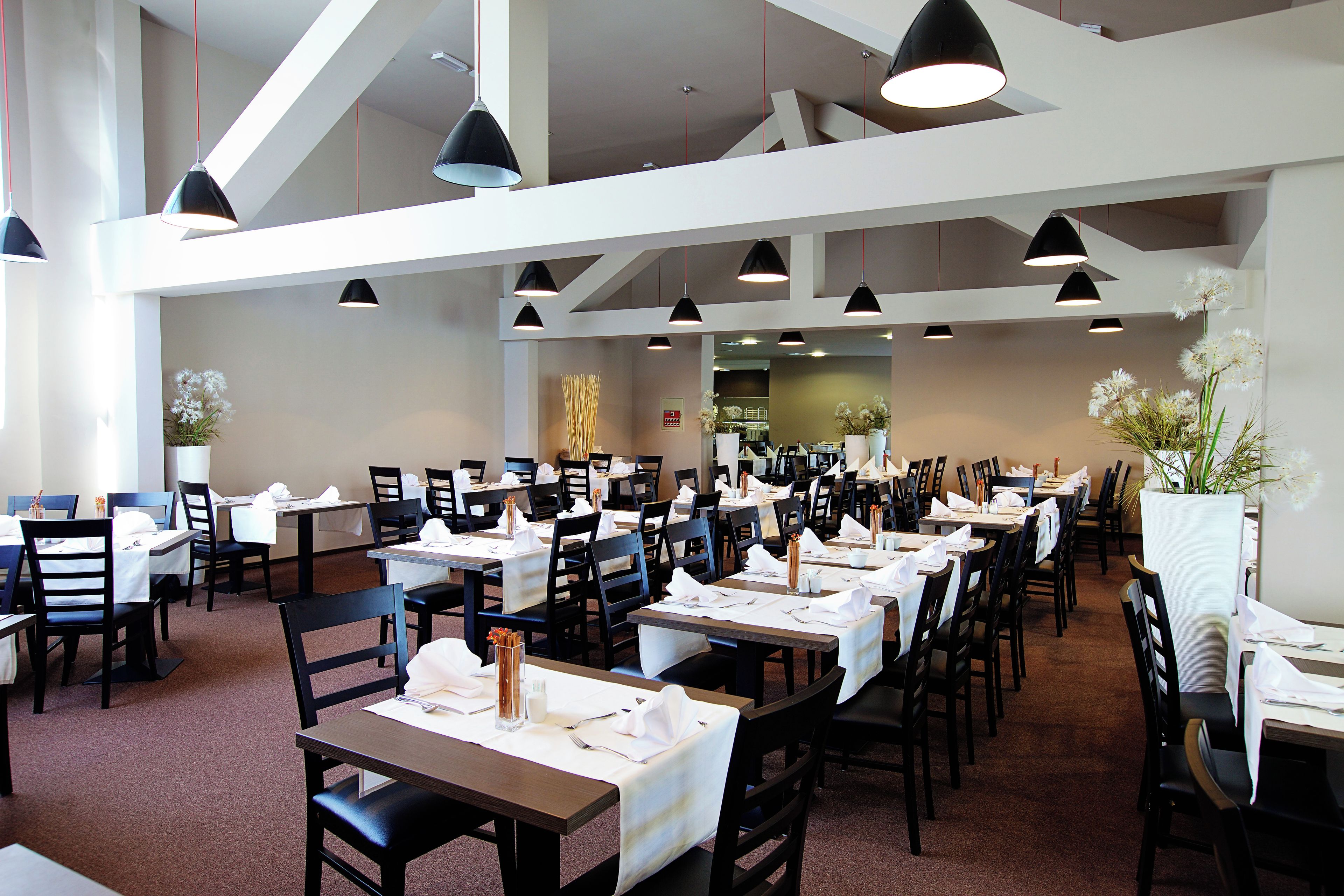 A spacious restaurant with multiple tables and chairs, pendant lighting, and a neutral color scheme.