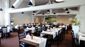 Un espaiós restaurant amb nombroses taules i cadires, sostres alts i il·luminació penjant.