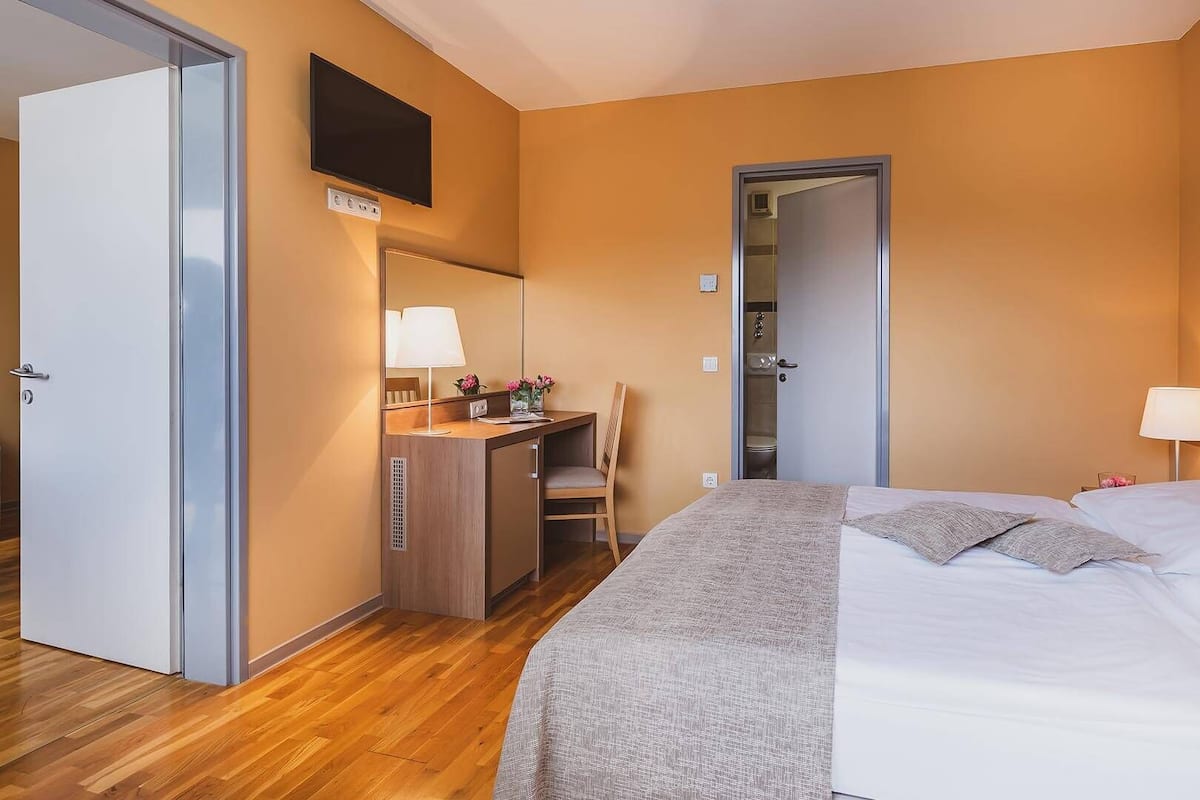 Una habitación de hotel con cama, escritorio, silla, televisor y puerta de baño.