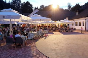 An outdoor café with multiple white umbrellas and tables, surrounded by brick pavement and buildings. - Hotel Breza (Podcetrtek)