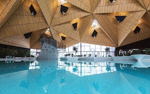 Una piscina con diseño geométrico del techo de madera y paredes de vidrio transparente.