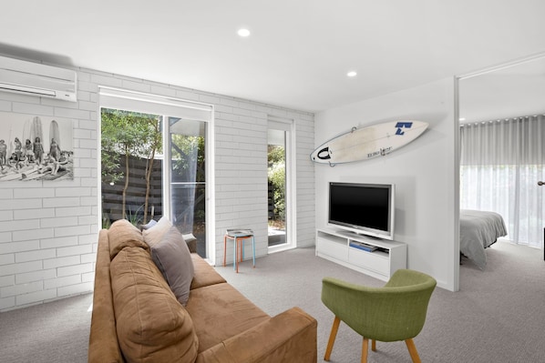 A modern living room with a large TV, a sofa, a green chair, and a surfboard on the wall.