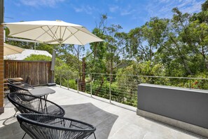 An outdoor patio area with a table and chairs, a large umbrella, and a view of trees and a fence. - One At Eight (Lorne)