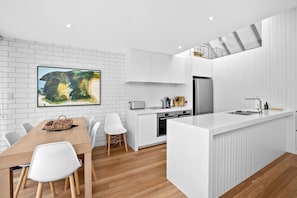 A modern kitchen with white cabinetry, a central island, and a dining area with a wooden table and white chairs.