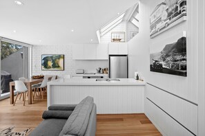 Eine moderne Küche mit weißen Schränken, einer zentralen Kochinsel und einem Essbereich mit einem grauen Sofa.