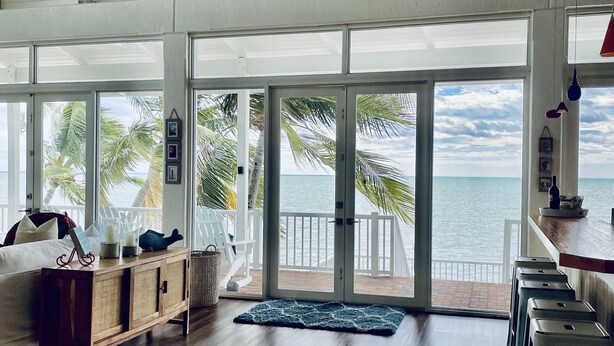 A spacious room with a wooden floor, a white ceiling, and large sliding glass doors leading to a balcony with a view of the ocean. - Beach Dream House, relax and enjoy the clear waters of Islamorada  FL  (Islamorada)