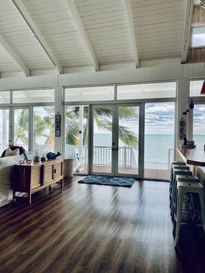 A spacious room with a wooden floor, a white ceiling, and large sliding glass doors leading to a balcony with a view of the ocean. - Beach Dream House, relax and enjoy the clear waters of Islamorada  FL  (Islamorada)