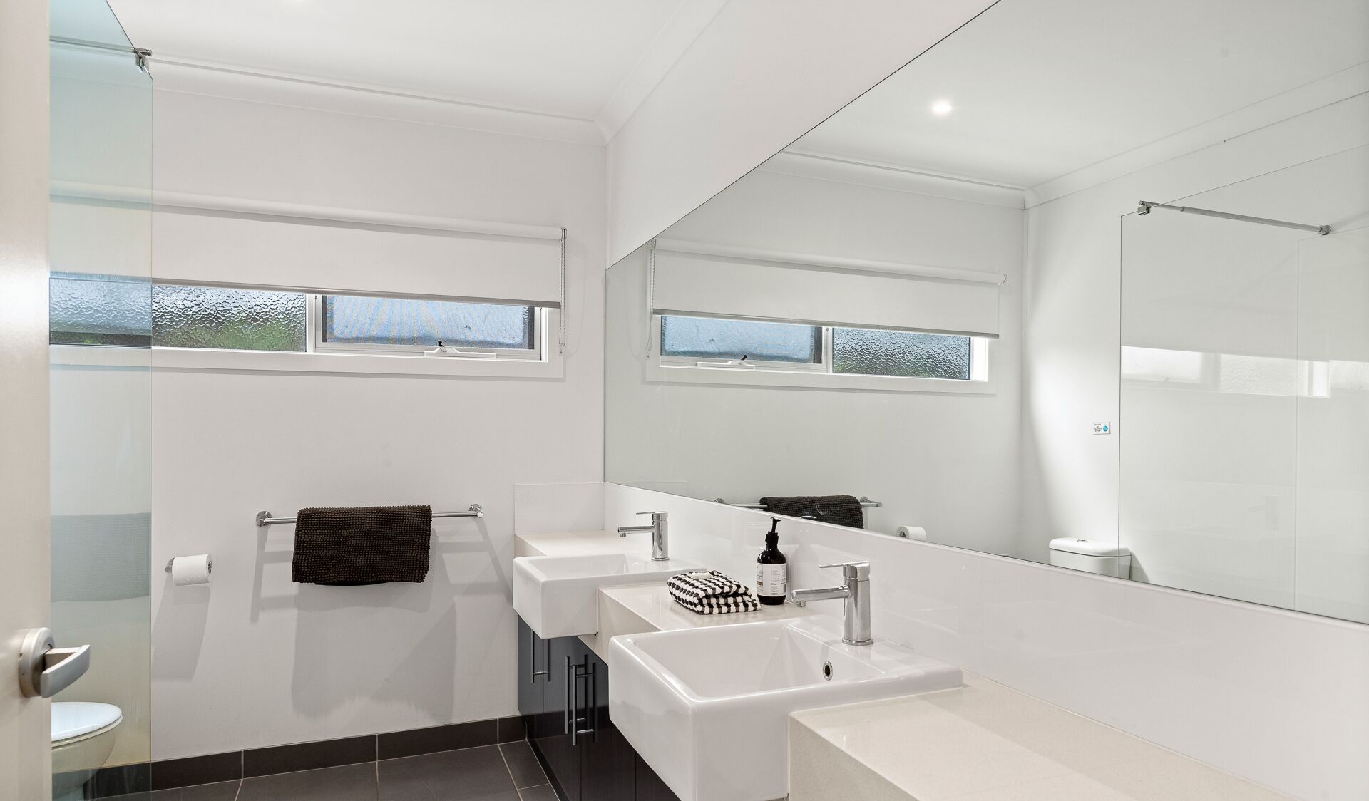 Une salle de bain moderne avec deux lavabos, un grand miroir et une fenêtre.
