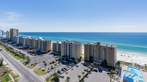 A beachfront hotel with multiple high-rise buildings, a parking lot, and a beach in the background.