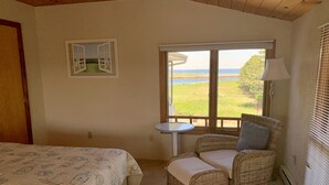 Een kamer met twee bedden, een rieten stoel, een tafeltje en een raam met uitzicht op een landschap.