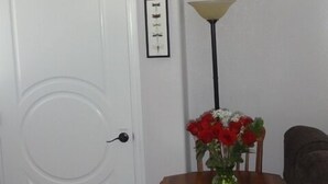 A dining area with a table and chairs, a vase of flowers, a lamp, and framed pictures on the wall.