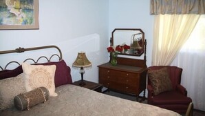 A bedroom with a bed, a dresser, a chair, a lamp, a mirror, and a painting on the wall.