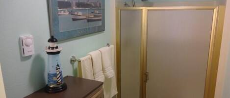 A bathroom with a wooden cabinet, a towel rack with a white towel, a glass shower enclosure, and a framed picture of boats on the wall.