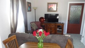 A dining area with a wooden table, chairs, and a vase of red flowers.