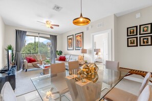 A modern living room with a glass dining table, sofas, and a ceiling fan.